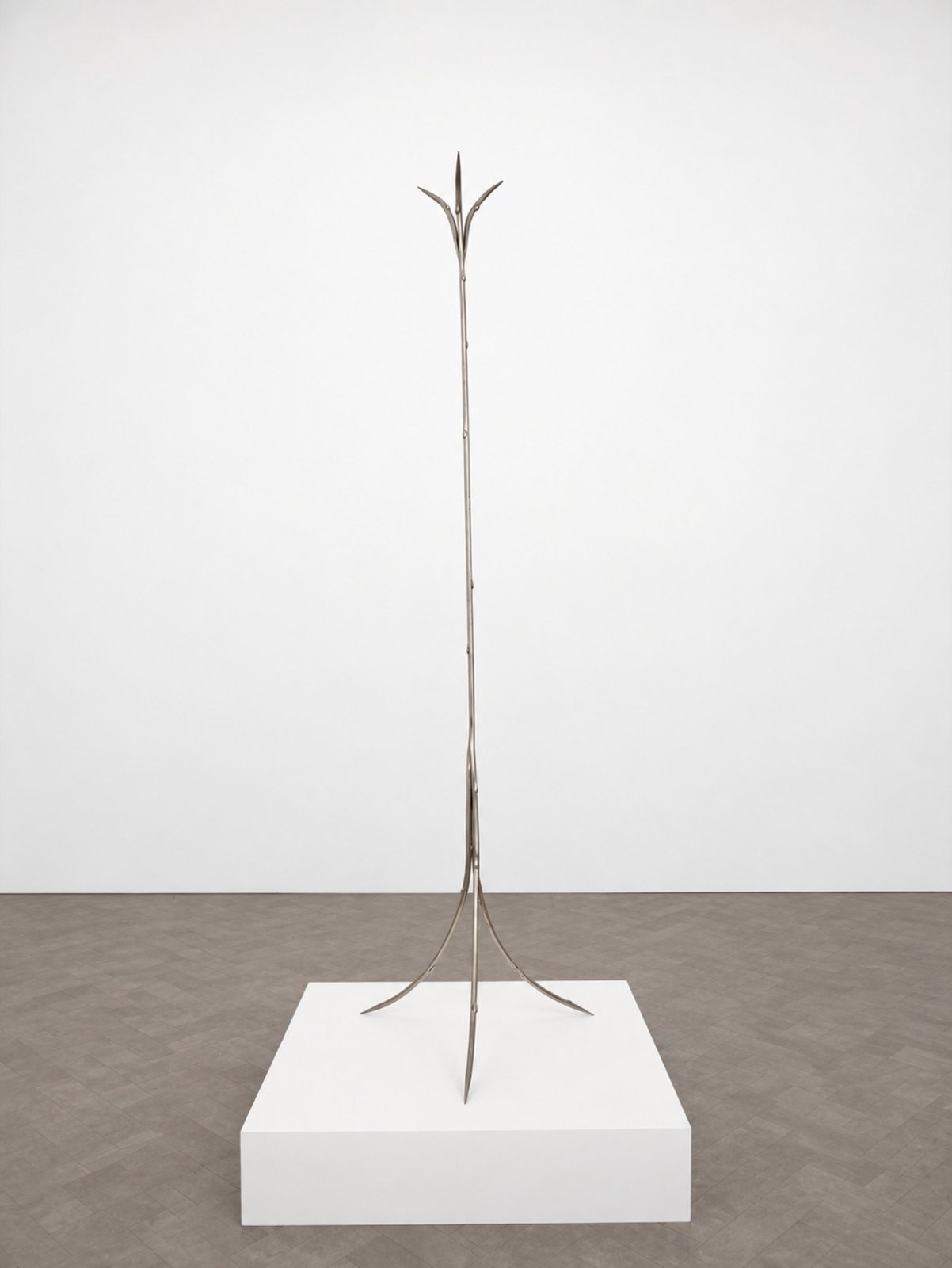 A tall, thin steel coat rack on a white plinth, its top opening like a flower.