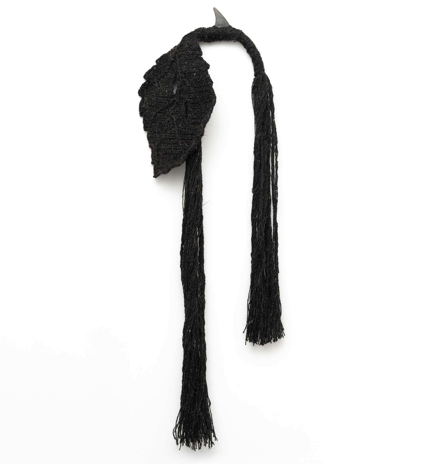 A black woollen leaf hung from a steel point, its long strands falling to a fringe.