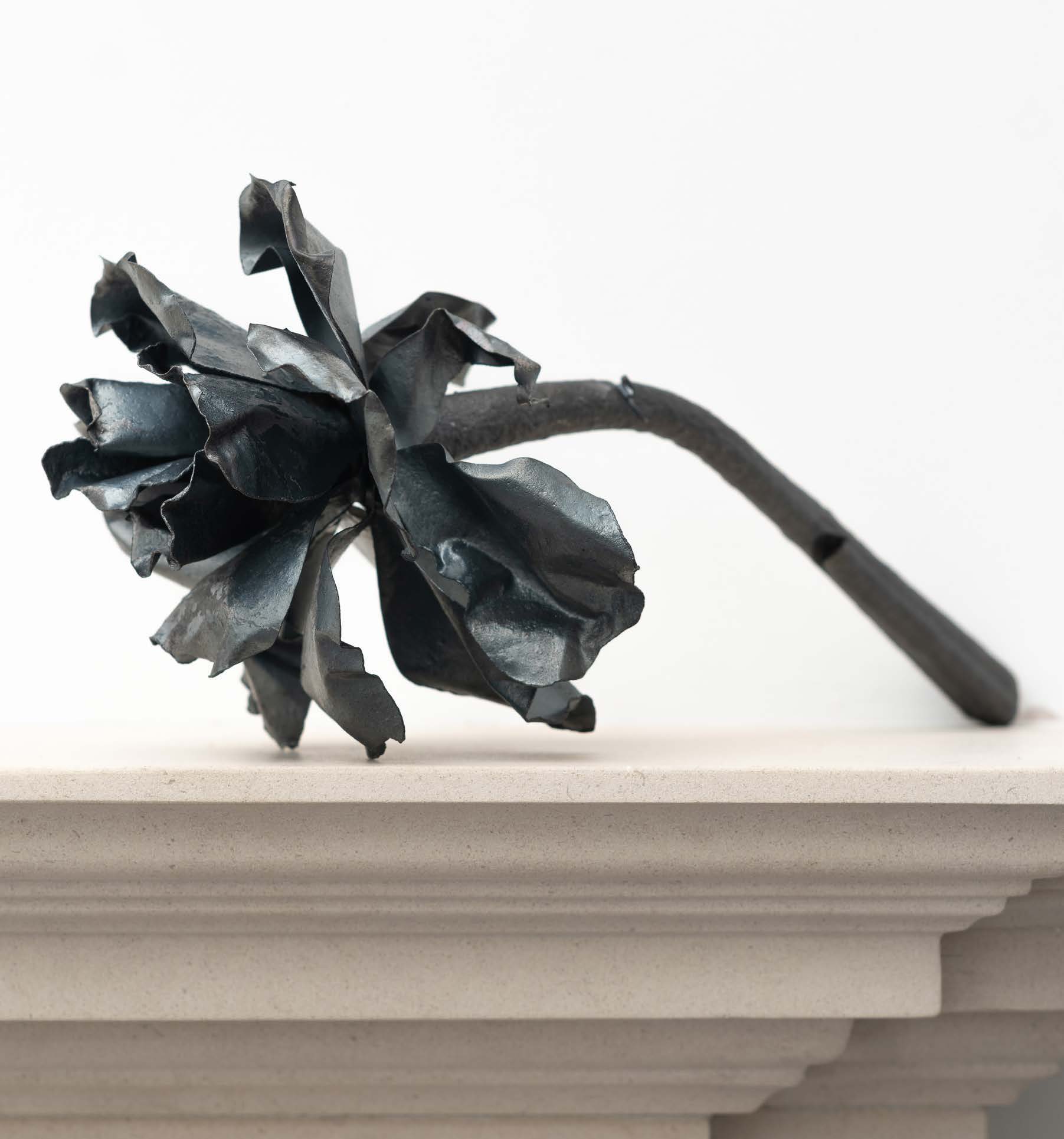 A dark steel flower lying across the edge of a mantelpiece.