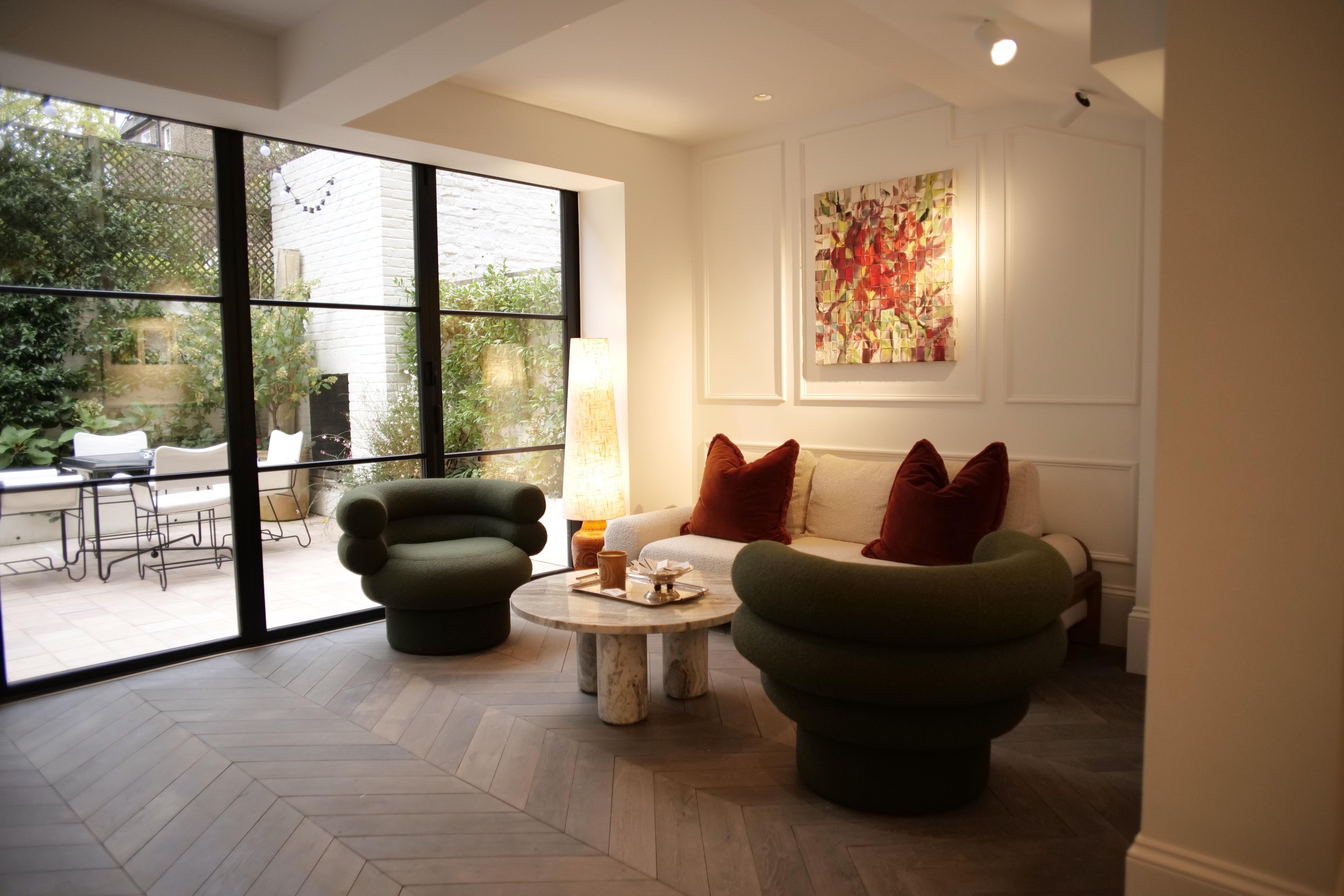 The living room at Gallery 44, with green armchairs, a sofa and glass doors opening onto the garden.
