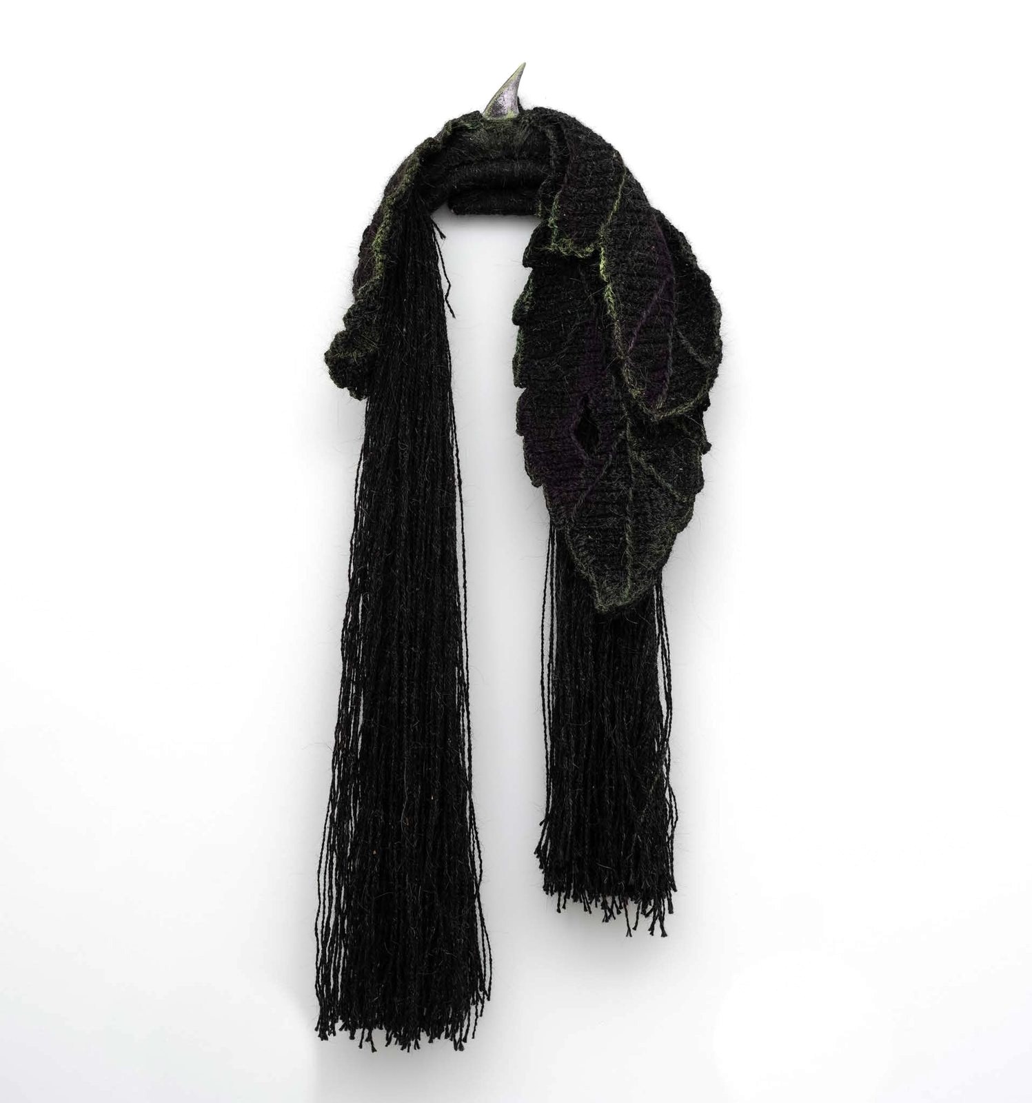 Dark woollen leaves draped over a steel point on the wall, with long goat-hair strands hanging below.