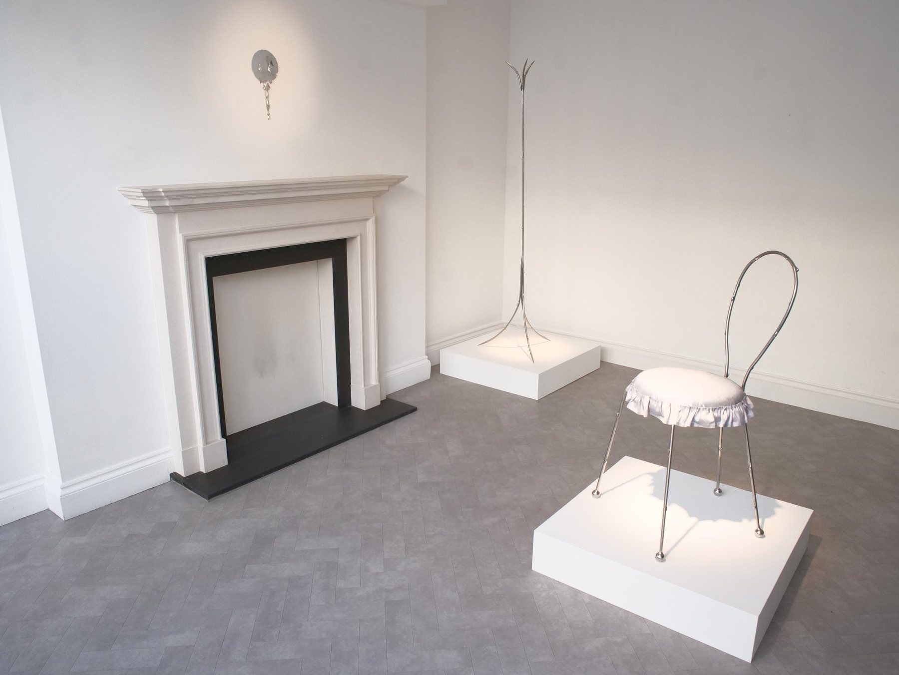 The front room by day: the chair and coat rack on white plinths, the mirror above the fireplace.