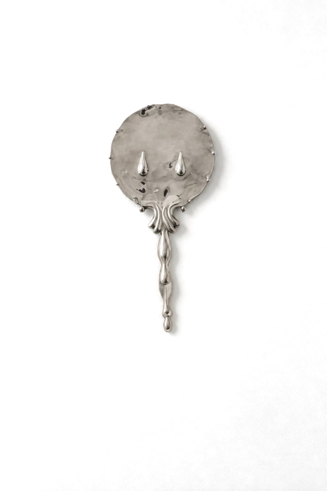 A silver-plated hand mirror hammered with raised tears, with an ornate handle.