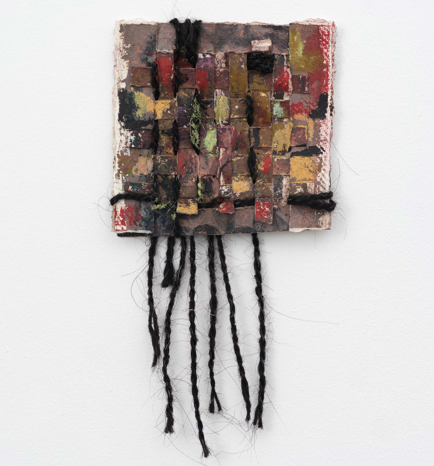 A small dark woven square with black strands hanging below.