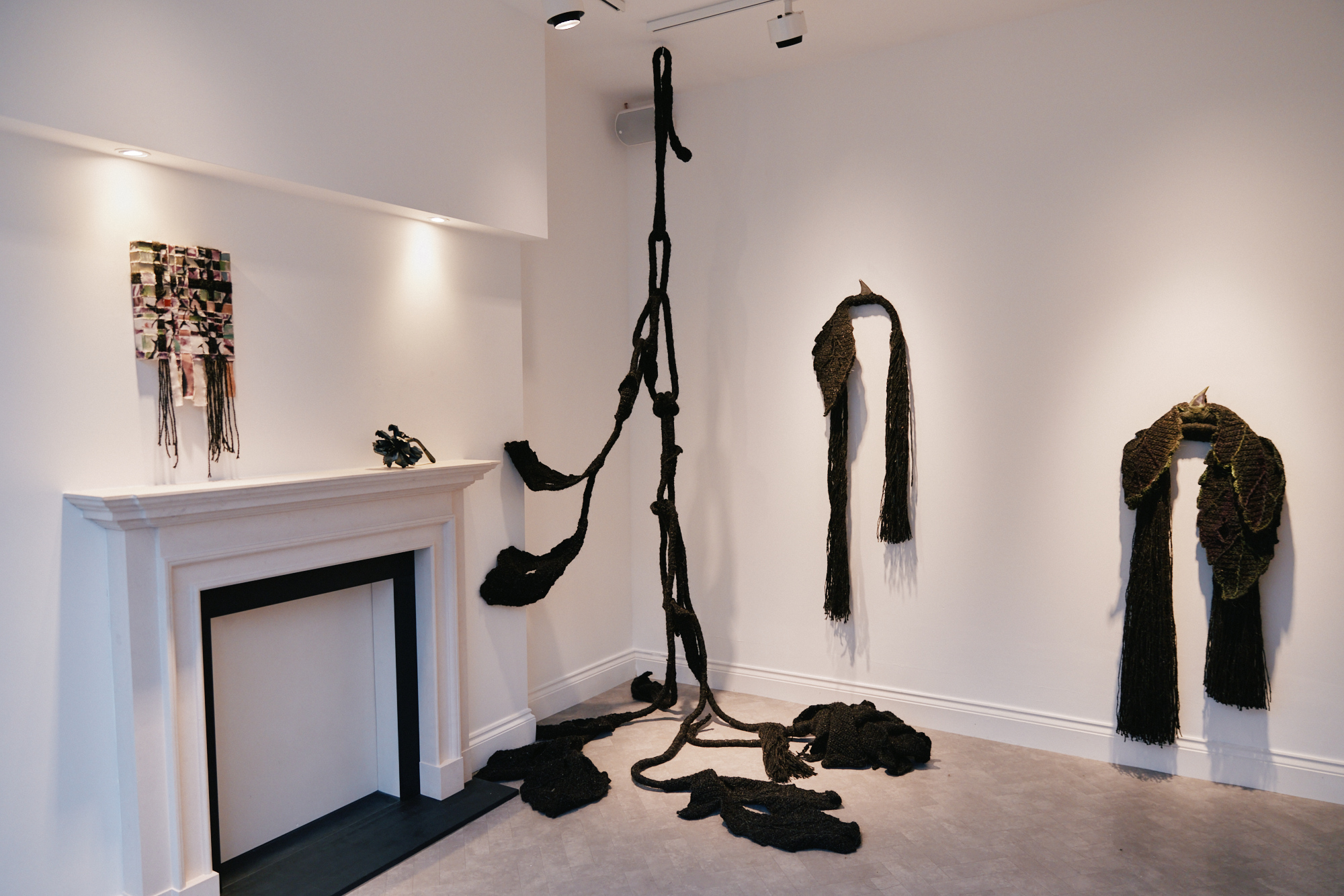 The Stasis installation around a white fireplace, with dark hanging and floor sculptures.